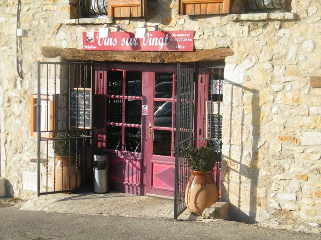 La façade en pierre du restaurant, avec sa porte rose, ses plantes et sa terrasse devant